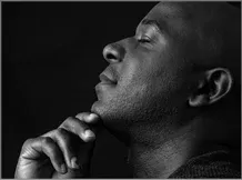 Black man elevating his head with hand on chin and eyes closed in deep thought.