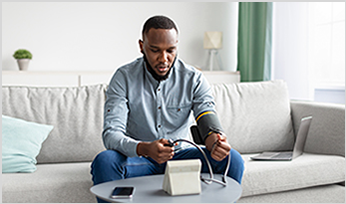Young black male taking blood pressure while sitting on couch - Preventing Stroke thumbnail graphic