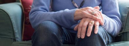 Older woman with hands crossed over legs. Focus On Parkinson's Disease banner image.