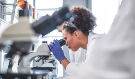 Researcher in lab looking into microscope.