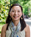 Smiling woman outdoors wearing a sleeveless top and patterned scarf.