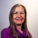 Woman with long gray-brown hair wearing a purple top.