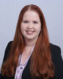 Woman with long red hair wearing a dark blazer.