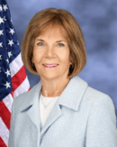 Woman in a light blue jacket with a U.S. flag in the background.