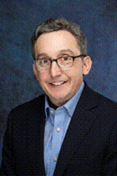 Man with glasses wearing a dark jacket and blue shirt.