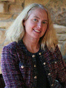 Woman with blonde hair wearing a textured jacket, seated indoors.