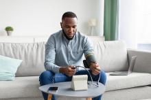 Young black male sitting on couch taking blood pressure as prevention against stroke..