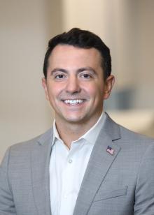 headshot of man with brown hair wearing a grey suit and white shirt