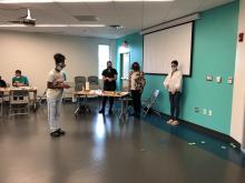 NINDS staff volunteers watch a teenager participate in the prism goggles activity at the Prince George’s County Memorial Library System’s STEM Fair.