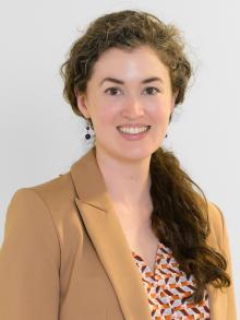 An image of a white woman with brown eyes and curly brown hair wearing a camel-colored blazer