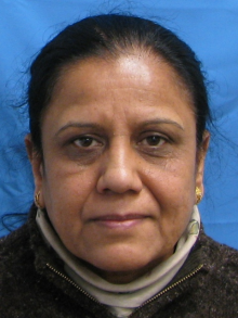 A woman with black hair wearing a brown jacket, smiling softly at the camera.
