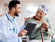 A doctor shows an older woman a tablet as they smile and talk together.
