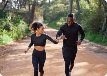Photograph of a young woman and young man running on a wooded path and checking their wristwatch heart rate monitors