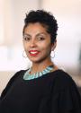 photo of a brown-skinned, short-haired woman wearing a black top, turquoise necklace, hoop earrings, and red lipstick