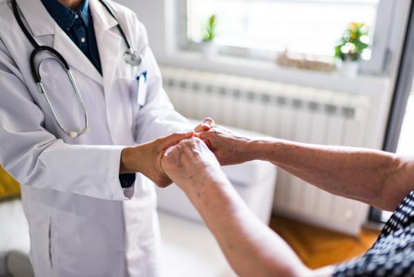 A doctor holds an older patient’s hands in a medical office.
