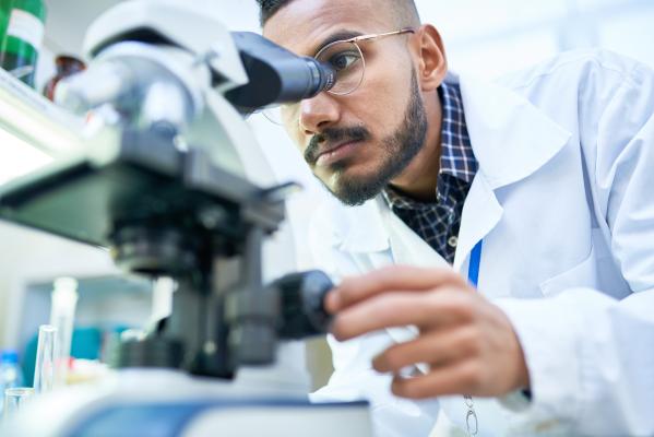 A scientist looks through a microscope in a lab.