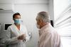 Masked doctor speaks with older masked patient